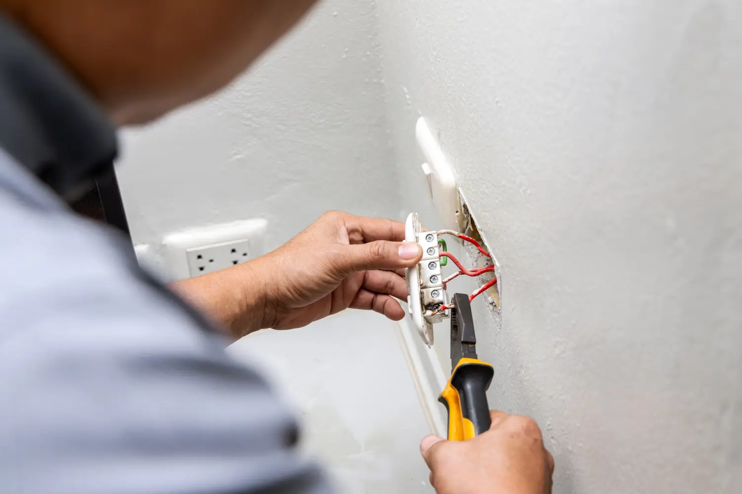 Nahaufnahme der Hand eines Elektrikers, der einen Steckdosenstecker zur Reparatur oder Wartung und Reparatur im Büroraum hält. Es besteht die Gefahr elektrischer Funken durch Kurzschlüsse und Feuer im Haus